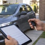 Persona revisando documentación junto a un auto y sosteniendo sus llaves