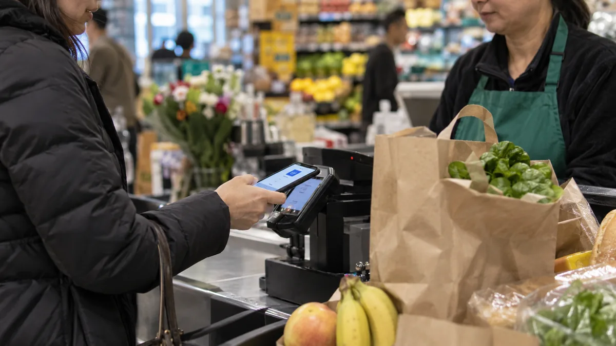 Cuenta dni: esta semana devuelve hasta $6. 000 por persona en compras de todos los días 2 Persona pagando con el celular en la caja de un comercio con bolsas de compras