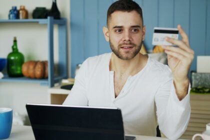 Persona sostiene una tarjeta de pago frente a una computadora portátil mientras realiza compras por internet, imagen ilustrativa