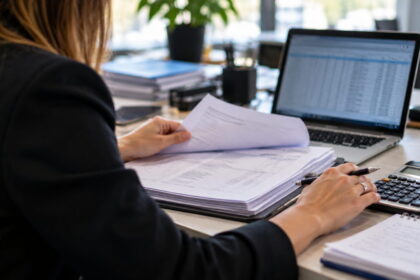 Empleada administrativa revisa documentación laboral y liquidaciones junto a una computadora en una oficina
